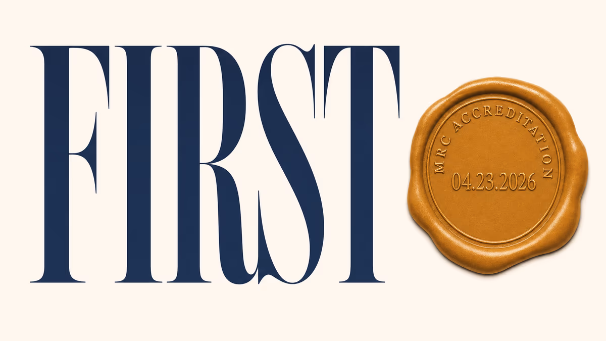 Tall navy serif word FIRST on warm ivory beside an amber wax-seal stamp legending MRC ACCREDITATION 04.23.2026.